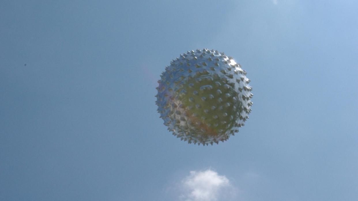  a silver balloon rises into a blue sky 