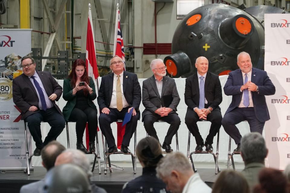 Representatives from all three levels of government, including Energy Minister Todd Smith (right) sit on stage in front of one of BWXT's large nuclear steam boilers.