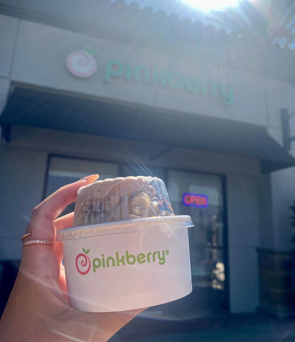 Melissa holding a free Pinkberry swirl in front of a Pinkberry yogurt shop.