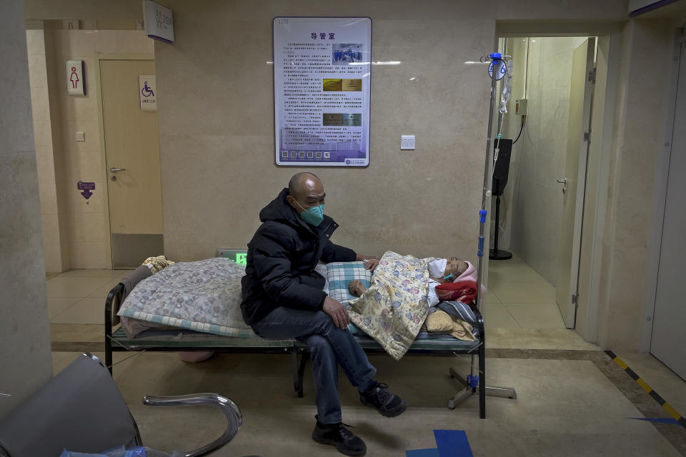 FILE - A man wearing a face mask tends to his elderly relative resting in a corridor of the emergency ward to receive an intravenous drip at a hospital in Beijing, Jan. 3, 2023. China's sudden reopening after two years holding to a "zero-COVID" strategy left older people vulnerable and hospitals and pharmacies unprepared during the season when the virus spreads most easily, leading to many avoidable deaths, The Associated Press has found. (AP Photo/Andy Wong, File)
