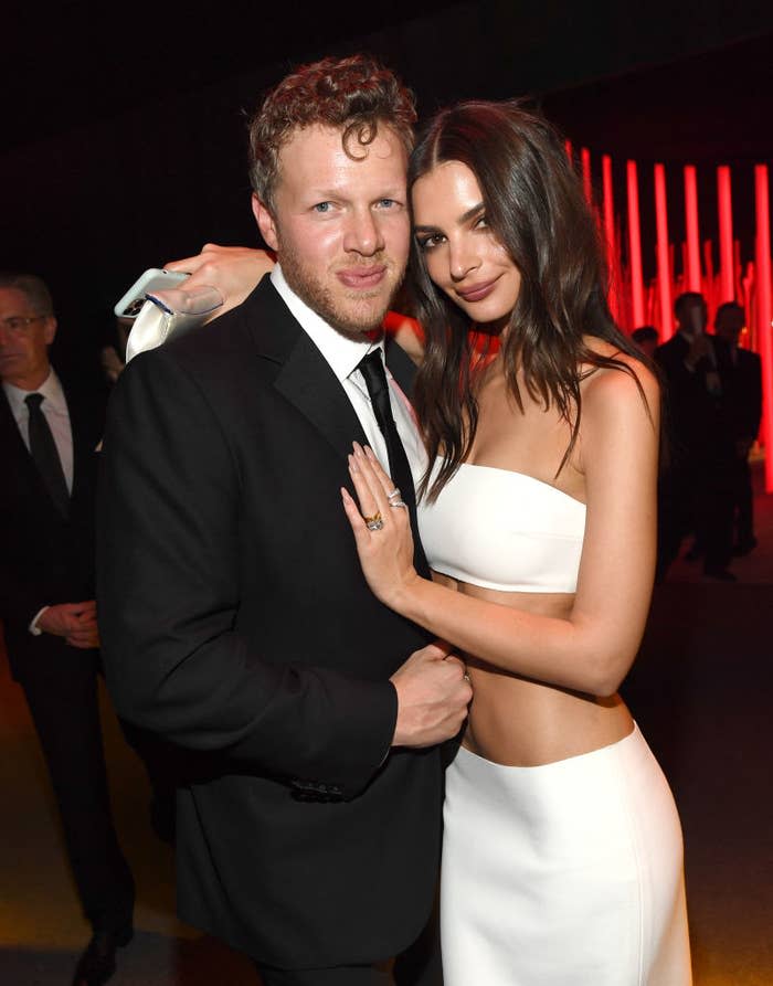 Two people embracing and smiling at the camera, one in a black suit, the other in a white strapless top and skirt