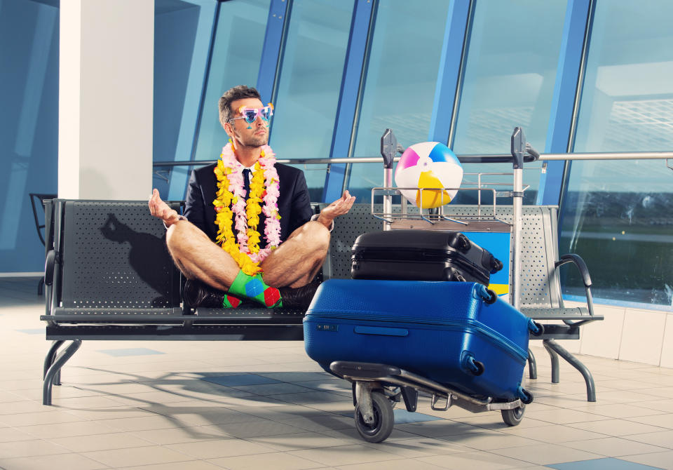 Portrait of businessman in a vacation mood, wearing beach shorts, garlands and sunglasses, sitting in yoga pose and waiting for the flight at the airport.