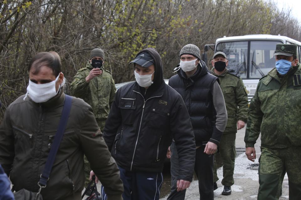 Ukrainian war prisoners, wearing face masks to protect against coronavirus, escorted by Russia-backed separatist soldiers, also wearing face masks to protect against coronavirus, walk to be exchanged near the checkpoint Horlivka, eastern Ukraine, Thursday, April 16, 2020. Ukrainian forces and Russia-backed rebels in eastern Ukraine have begun exchanging prisoners in a move aimed at ending their five-year long war. (AP Photo/Alexei Alexandrov)