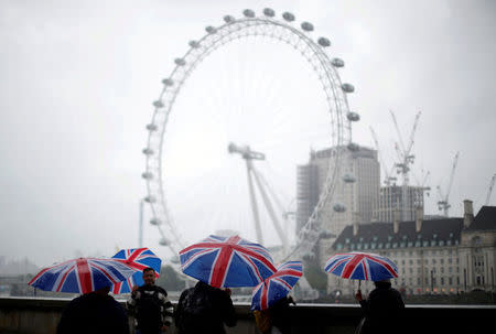 FILE PHOTO: Tourists carrying Union Flag umbrellas shelter from the rain in front of the London Eye wheel in London, Britain, August 9, 2017. REUTERS/Hannah McKay/File Photo