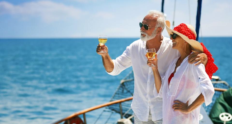 Two seniors on a sailboat toasting with drinks while looking out to sea.