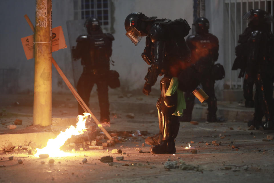 Riot police put out a petrol bomb hurdled during clashes with anti-government demonstrators protesting against the FIFA World Cup Qatar 2022 qualifying soccer match between Argentina and Colombia near the Metropolitano stadium in Barranquilla, Colombia, Tuesday, June 8, 2021. (AP Photo/Jairo Cassiani)