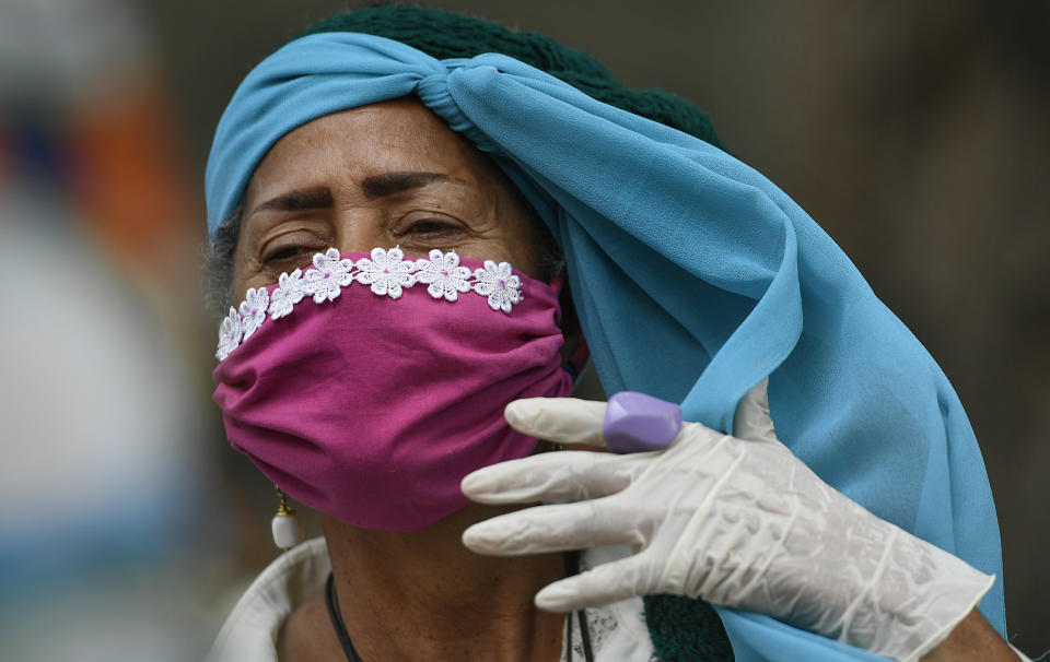 Una anciana que usa una mascarilla protectora y guantes desechables se ajusta el pañuelo en la cabeza mientras camina afuera en un hogar de ancianos en medio de la propagación del nuevo coronavirus en Caracas, Venezuela, el sábado 2 de mayo de 2020. (AP Foto / Matias Delacroix)