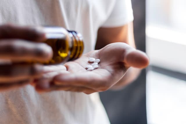 <p>Malorny / Getty Images</p> Young male spilling multiple pills in his hand.