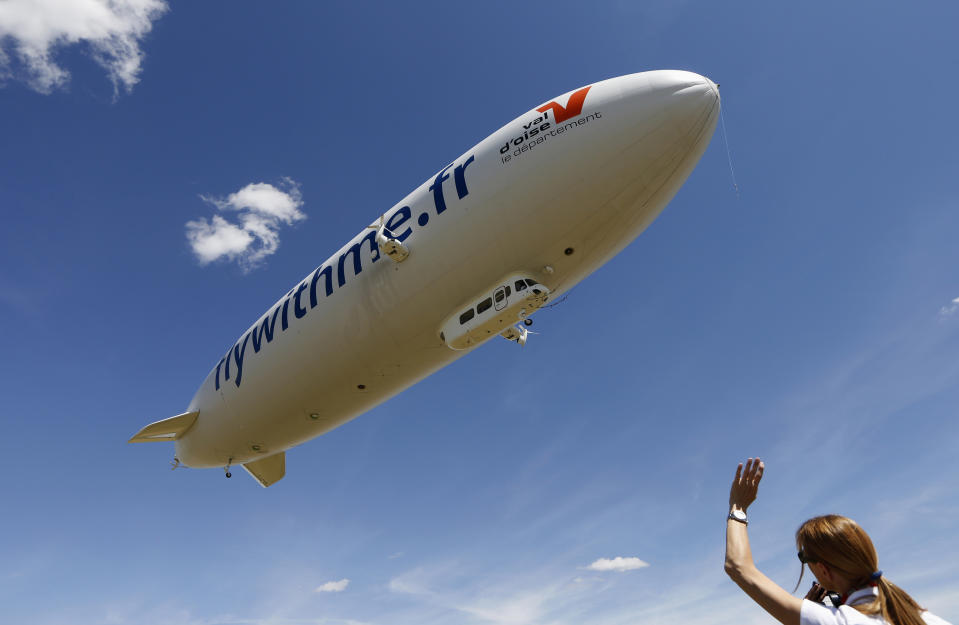 A ground crew member waves as a semi-rigid and helium-filled Zeppelin NT departs from a field at an airport outside Cergy-Pontoise, near Paris, August 4, 2013. The Zeppelin NT is powered by three pivoting motors and measures 75.1 meters (246 ft) long, (as long as an Airbus 380), 17.4 meters (57 feet) high, and 19.5 (64 feet) meters wide. It also has a cabin that fits 12 passengers and will fly tourists at an altitude of 300 meters (984 feet) over the countryside. According to the company's media release, Airship Paris, which runs the Zeppelin NT, will propose three different flights for tourists in the Paris region, including the Chateau of Versailles, Giverny, and Chantilly and the valley of the Impressionists.   REUTERS/John Schults   (FRANCE - Tags: TRANSPORT SOCIETY TRAVEL TPX IMAGES OF THE DAY)