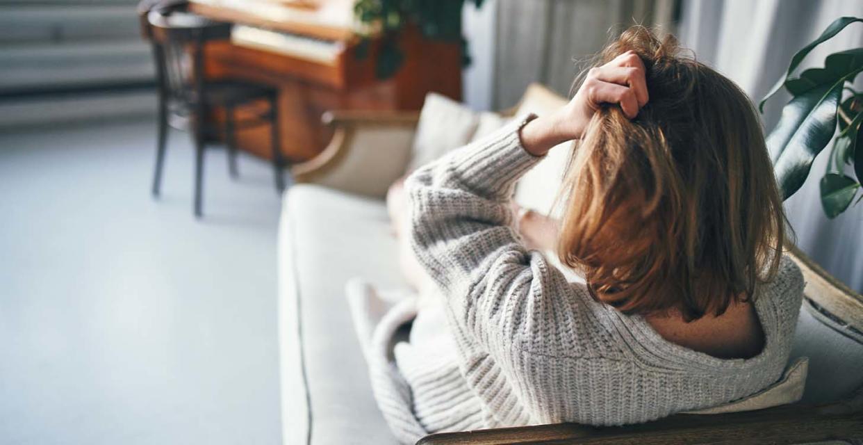 Someone sitting on couch, seen from behind, clutching their hair with left hand.