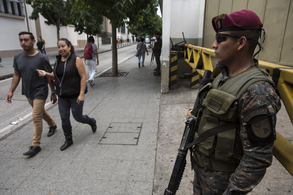 People walk past a Presidential House as soldiers stands guard, one day before the general elections, in the historic district of Guatemala City, Saturday, June 15, 2019. The road to Sunday's presidential election in Guatemala has been a chaotic flurry of court rulings and shenanigans, illegal party-switching and allegations of malfeasance that torpedoed the candidacies of two of the top three candidates. (AP Photo/Oliver de Ros)