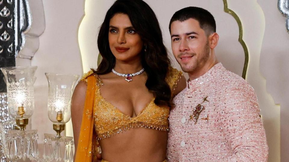 Priyanka Chopra and her husband Nick Jonas are both dressed in lavish wedding outfits, smiling at the cameras.