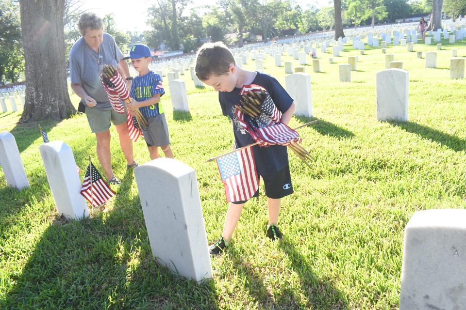 Cindy Green (far left) shows her grandsons Crosstin Green and Jayse Hattaway how to properly place flags on gravesites at Alexandria National Cemetery in Pineville. The flags were placed in preparation for the Memorial Day program set for Monday.