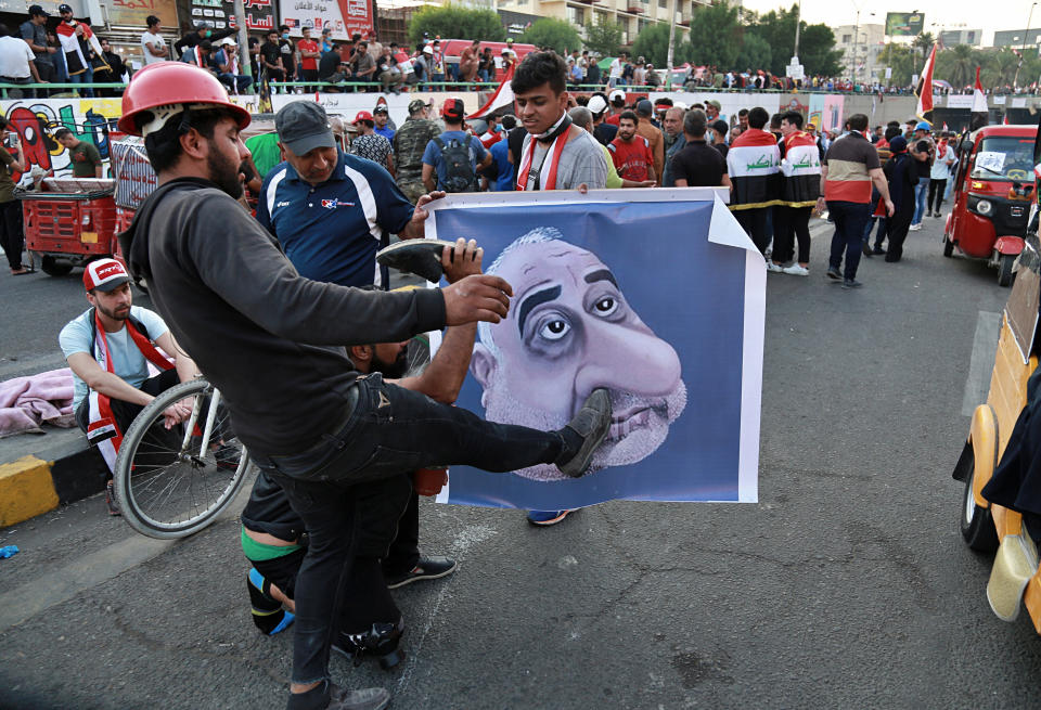 FILE - in this Sunday, Nov. 3, 2019 file photo, protesters hit a poster showing Iraqi Prime Minister Adel Abdel-Mahdi with shoes during ongoing anti-government protests in Baghdad, Iraq. Iraqi Prime Minister Adel Abdul-Mahdi said Friday, Nov. 29, he would submit his resignation to parliament, a day after more than 40 people were killed by security forces and following calls by Iraq's top Shiite cleric for lawmakers to withdraw support. (AP Photo/Khalid Mohammed, File)