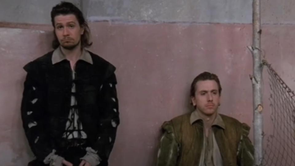 Gary Oldman standing and Tim Roth sitting against a wall in Rosencrantz & Guildenstern Are Dead.