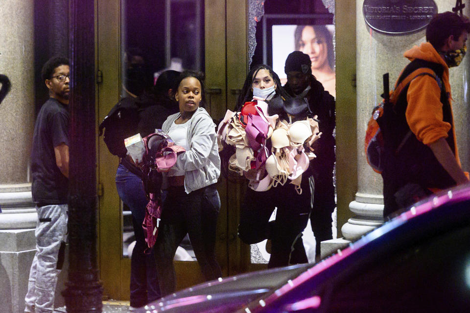 FILE - In this May 30, 2020, file photo, women carry merchandise from a Union Square Victoria's Secret store in San Francisco. Police say many of the smash-and-grab thefts have been carried out by caravans of well-coordinated criminals that have coincided with or followed protests over the death of George Floyd, who was killed by a Minneapolis police officer who pressed his knee into Floyd's neck. (AP Photo/Noah Berger, File)