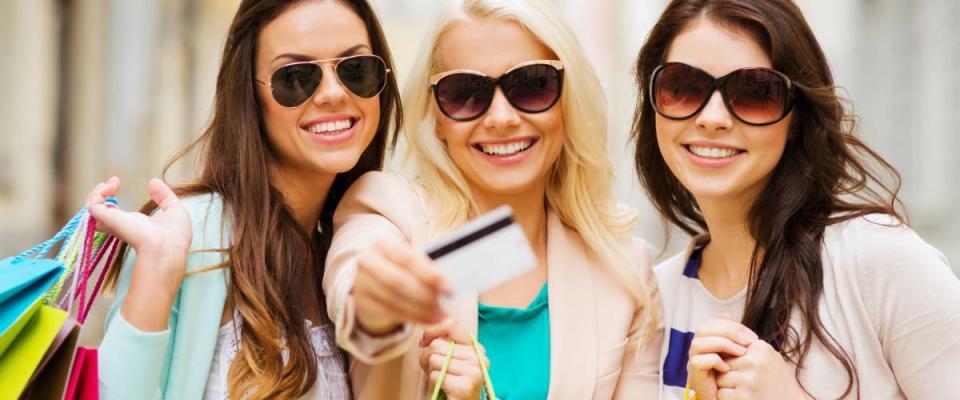 shopping and tourism concept - beautiful girls with shopping bags and credit card in ctiy