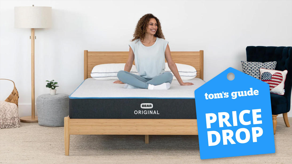  Bear Original Mattress image shows a woman with curly dark hair smiling and sitting cross-legged on the mattress, while a blue price drop sales badge overlaid on the image. 