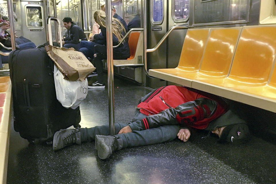 FILE - A man sleeps under the seats of a subway car in New York on Oct. 31, 2017. Democratic leaders in major U.S. cities are finding themselves politically squeezed when it comes to addressing homelessness. New York Mayor Eric Adams, who has hailed his city’s right to shelter as a hallmark of compassion for its most destitute, must now decide if he will extend that compassion by bestowing homeless people with the right to sleep outside. (AP Photo/Richard Drew, File)