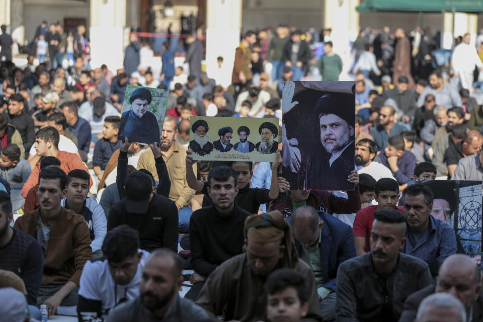 People hold up pictures of the Shiite cleric Muqtada al-Sadr during Friday prayers at a mosque in Kufa, Iraq, Friday, Dec. 2, 2022. Al-Sadr who announced his withdrawal from politics four months ago has broken a period of relative silence to launch an anti-LGBTQ campaign. (AP Photo/Anmar Khalil)