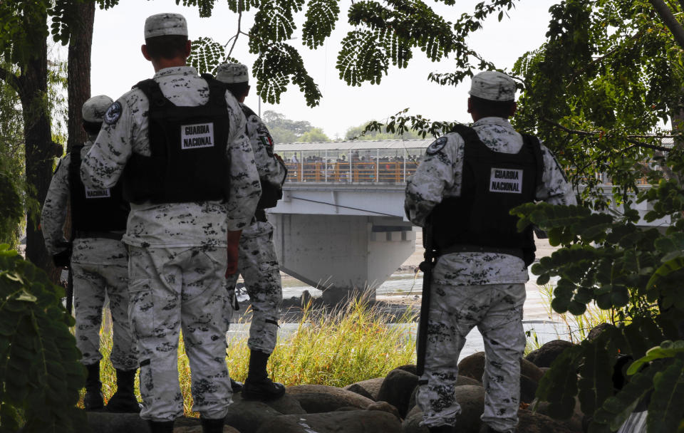 Varios efectivos de la Guardia Nacional de México observa una multitud de migrantes que pretenden cruzar un puente sobre el río Suchiate para cruzar hacia ciudad Hidalgo, México, desde Guatemala, el sábado 18 de enero de 2020. (AP Foto/Marco Ugarte)