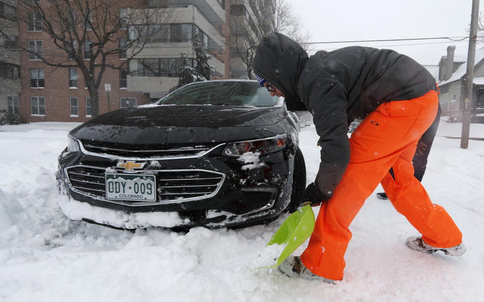 Erik Randa helps dig out a stuck Chevrolet Malibu being used by a ride-sharing service driver out of an intersection at 2nd Ave. and Pearl St. as a storm packing snow and high winds sweeps in over the region Tuesday, Nov. 26, 2019, in Denver. Stores, schools and government offices were closed or curtailed their hours while on another front, Thanksgiving Day travellers were forced to wrestle with snow-packed roads and flight delays or cancellations throughout the intermountain West. (AP Photo/David Zalubowski)