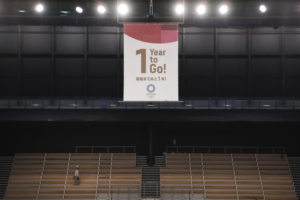 A worker walks near a "1-Year to Go" banner at the Ariake Gymnastics Center, Monday, July 22, 2019, in Tokyo. Despite scandals, rising costs and doubts about the economic payoff, the Tokyo Olympics will be a must-see event — if you can find a ticket or a hotel room — when they open in a year. Tokyo was supposed to be a "safe pair of hands" after Rio de Janeiro's corruption and near-meltdown three years ago. (AP Photo/Jae C. Hong)