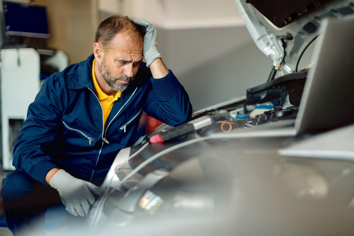 Displeased auto mechanic thinking while repairing engine of a car at repair shop.