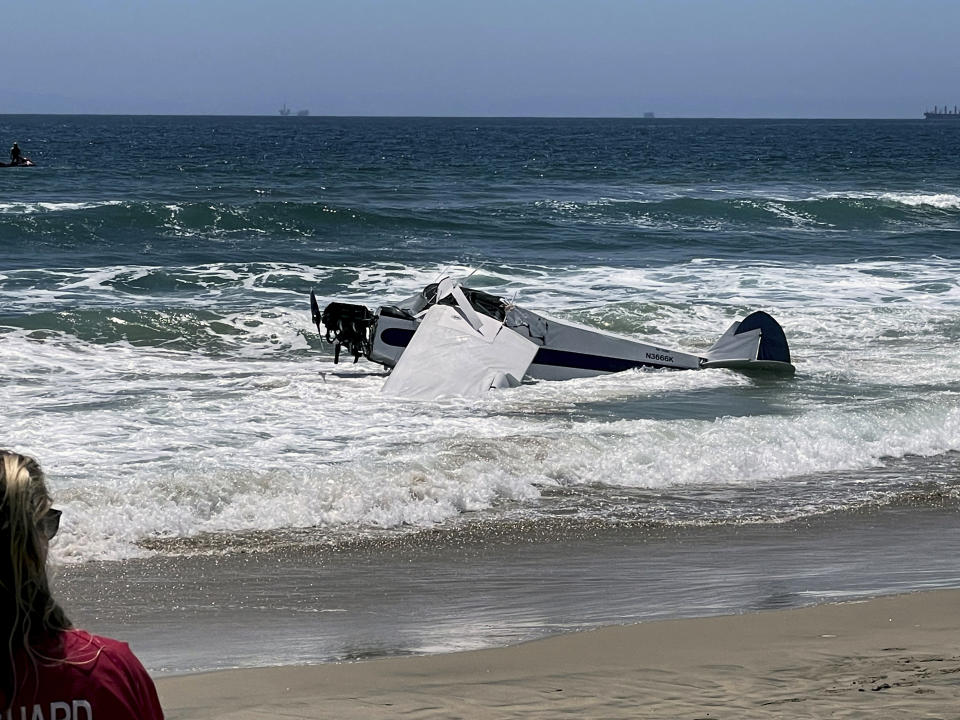 A small plane sits in the surf after it crashed into the ocean just off Huntington Beach, Calif. on Friday, July 22, 2022, during a lifeguarding competition. A Coast Guard spokesperson says the plane went down Friday about 30 yards from shore and the pilot was rescued. He was the only person aboard. (Corinne Baginski via AP)