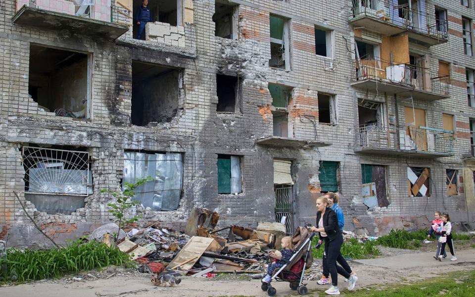 Locals walk past a building that was damaged during shelling in the outskirts of Kharkiv - SERGEY KOZLOV/EPA-EFE/Shutterstock 