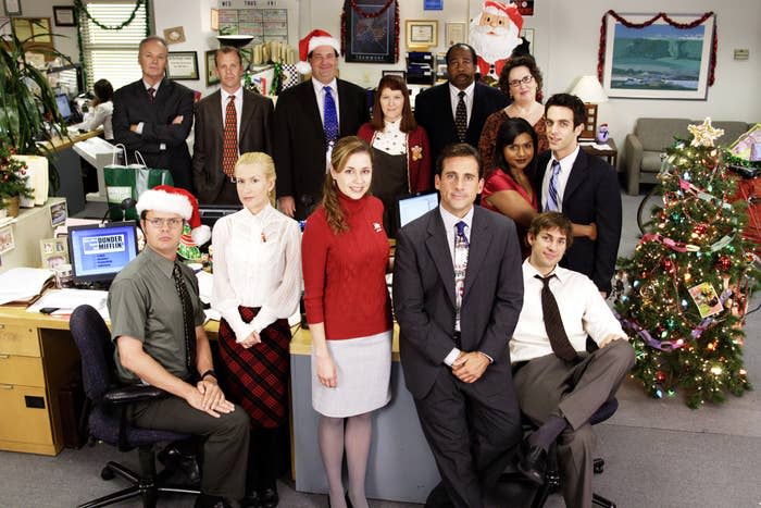 The entire Office cast poses near a desk, some have santa hats on