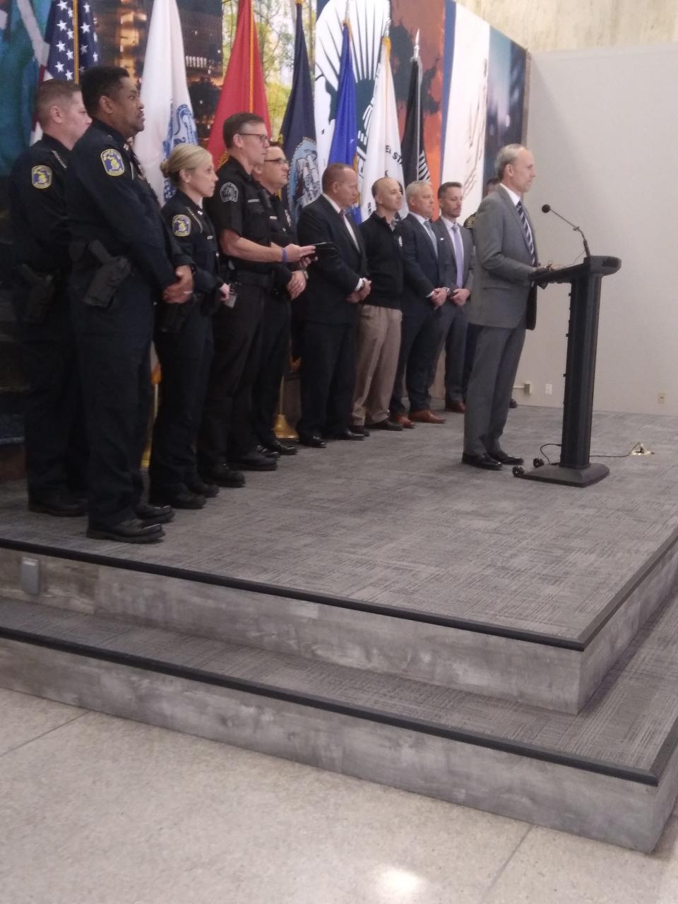U.S. District Attorney Mark Totten stands at a podium during a news conference Thursday, May 25, 2023 at Lansing City Hall, flanked by various state and local officials.