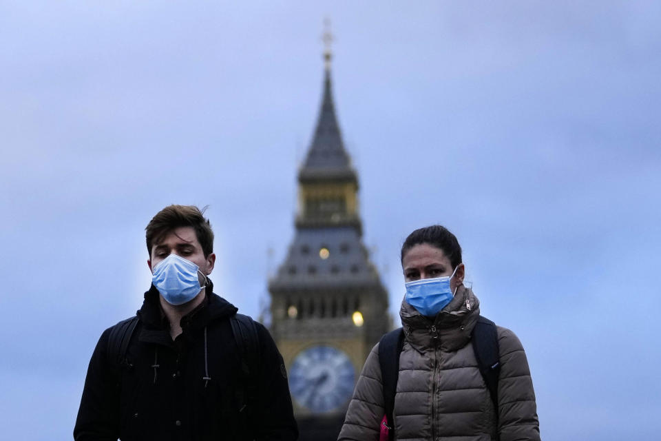 People wearing a face covering walk across Westminster Bridge in London, Wednesday, Dec. 15, 2021. As of Monday in England, people were urged to work from home if possible, with long lines forming at vaccination centers for people to get booster shots to protect themselves against the coronavirus omicron variant. (AP Photo/Frank Augstein)