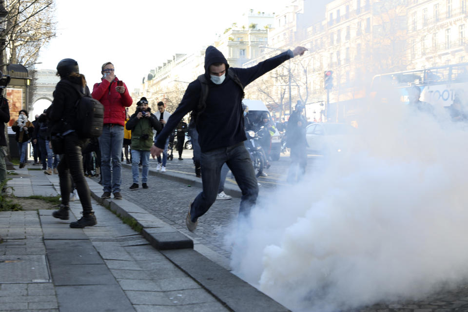 A demonstrator kicks in a tear gas grenade during a protest on the Champs-Elysees avenue, Saturday, Feb.12, 2022 in Paris. Paris police intercepted at least 500 vehicles attempting to enter the French capital in defiance of a police order to take part in protests against virus restrictions inspired by the Canada's horn-honking "Freedom Convoy." . (AP Photo/Adrienne Surprenant)