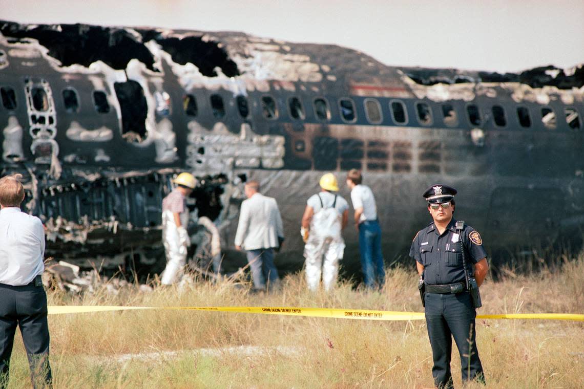 Aug. 31, 1988: A police officer stands in front of crime scene tape as firefighters and other emergency workers examine the charred fuselage of Delta 1141, which crashed that morning during takeoff at Dallas-Fort Worth International Airport.