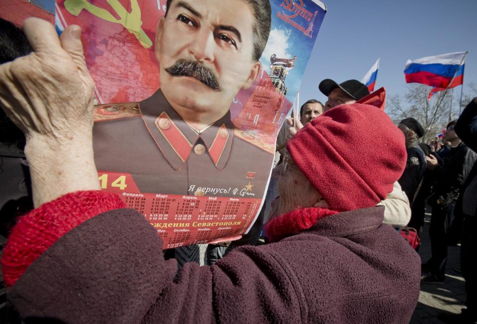 An elderly woman holds a calendar depicting Soviet leader Josef Stalin while watching a broadcast of Russian President Vladimir Putin's speech on Crimea in Sevastopol, Crimea, Tuesday, March 18, 2014, as thousands of pro-Russian people gathered to watch the address. Fiercely defending Russia's move to annex Crimea Putin said Russia had to respond to what he described as a western plot to take Ukraine into its influence.(AP Photo/Vadim Ghirda)