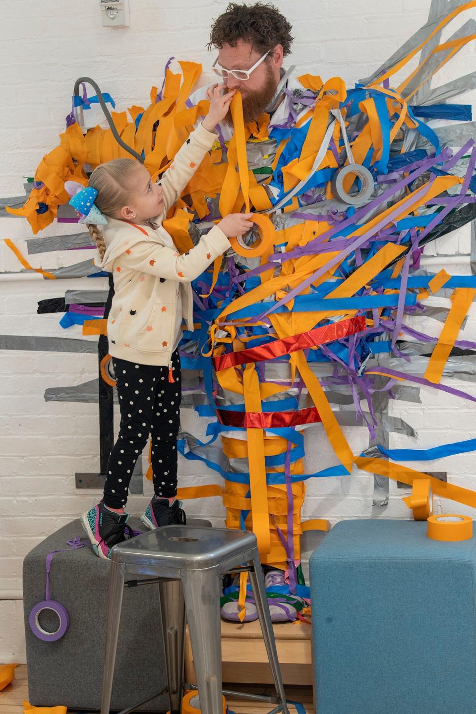 Emily Freshour of East Manchester Township, left, reached up to get one last piece of tape on Matthew Davis during the hour-long wall taping at Keystone Kidspace Monday.