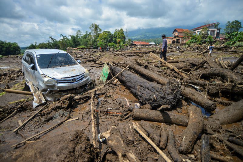 A man stands near a damaged car in an area area affected by heavy rain brought flash floods and landslides in Agam