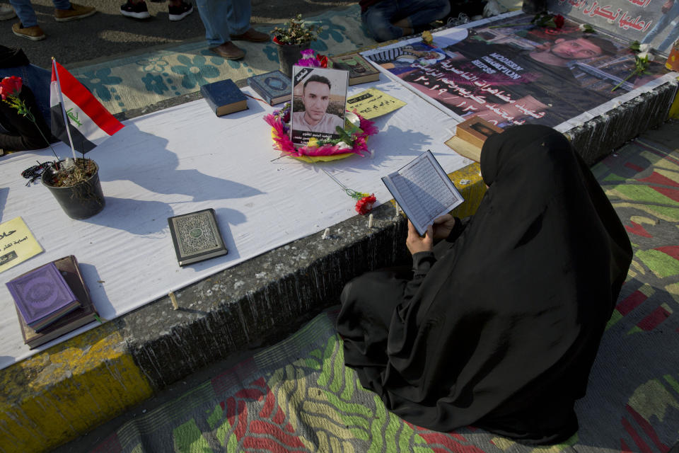 An Iraqi woman reads from the Quran by a stone memorial for killed protesters at Tahrir square, in Baghdad, Iraq, Sunday, Dec. 8, 2019. Arabic reads, "the Martyr of al-Nasseriyah protests Mohammed Karim Rahem al-Zameli, 12/5/2019." (AP Photo/Nasser Nasser)