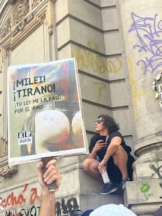 A protestor holding a placard  reading 'Tyrant Milei, I shove your laws up my arse'.