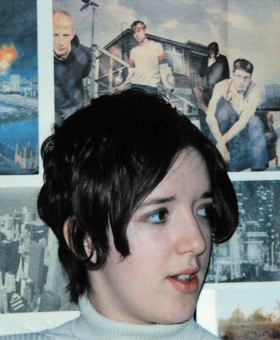 Anna Doble in the 1990s sitting in front of a Blur poster