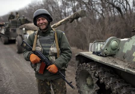 A member of the Ukrainian armed forces and armoured personnel carriers smiles as they prepare to move to pull back from Debaltseve region, near Artemivsk February 26, 2015. REUTERS/Gleb Garanich