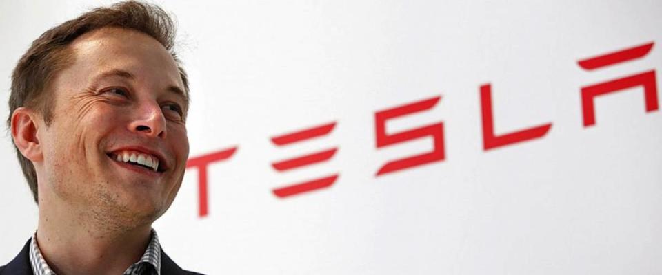 Elon Musk stands next to Tesla logo