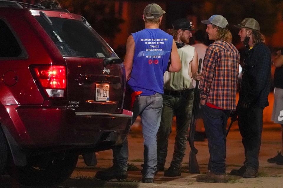 FILE - In this Aug. 25, 2020 file photo, a group holds rifles as they watch protesters on the street in Kenosha, Wis. Protests continued following the police shooting of Jacob Blake two days earlier. Kyle Rittenhouse is white. So were the three men he shot during street protests in Kenosha in 2020. But for many people, Rittenhouse's trial will be watched closely as the latest referendum on race and the American judicial system. (AP Photo/Morry Gash, File)