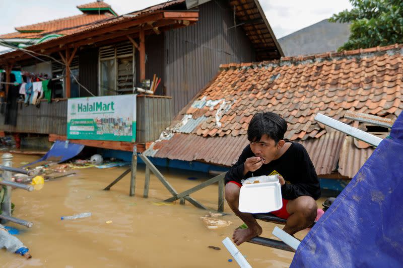 Muhamad Fathur Rizki, 19, eats his lunch outside his house, flooded after heavy rains in Jakarta