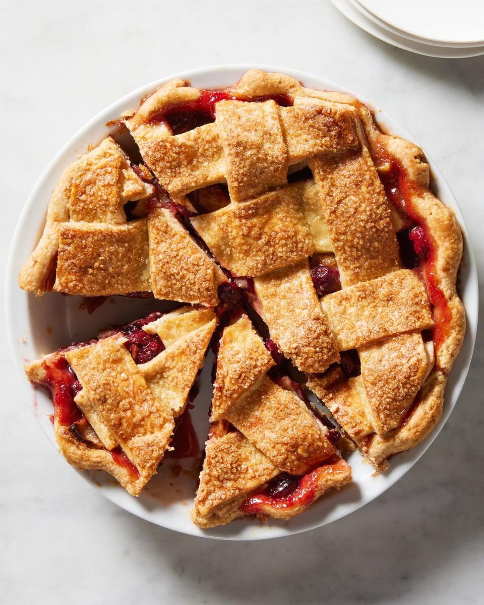 cranberry apple pie with topped with a lattice crust in a white pie pan with one slice cut out