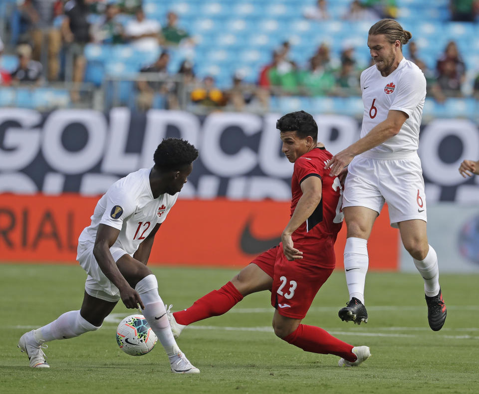 Cuba's Luis Paradela (23) tries to drives between Canada's Alphonso Davies (12) and Samuel Piette (6) during the first half of their CONCACAF Golf Cup soccer match in Charlotte, N.C., Sunday, June 23, 2019. (AP Photo/Chuck Burton)