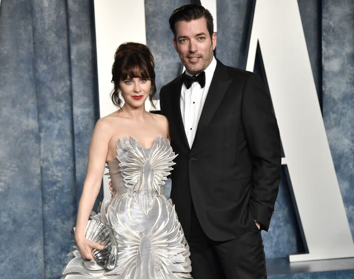 Zooey Deschanel in a strapless, silver gown standing next to Jonathan Scott in a suit