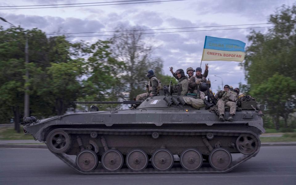 Ukrainian serviceman wave a flag reading "Glory to Ukraine", top, and "Death to the enemies" as they ride atop a tank in the Kharkiv region - Bernat Armangue /AP