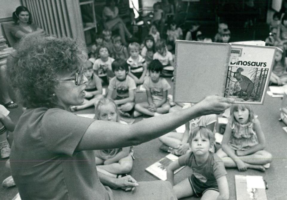 Teacher holding up a book about dinosaurs in class of young kids